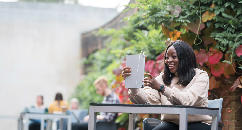 A student using a tablet in the Camper Coffee courtyard outside Queen's Building