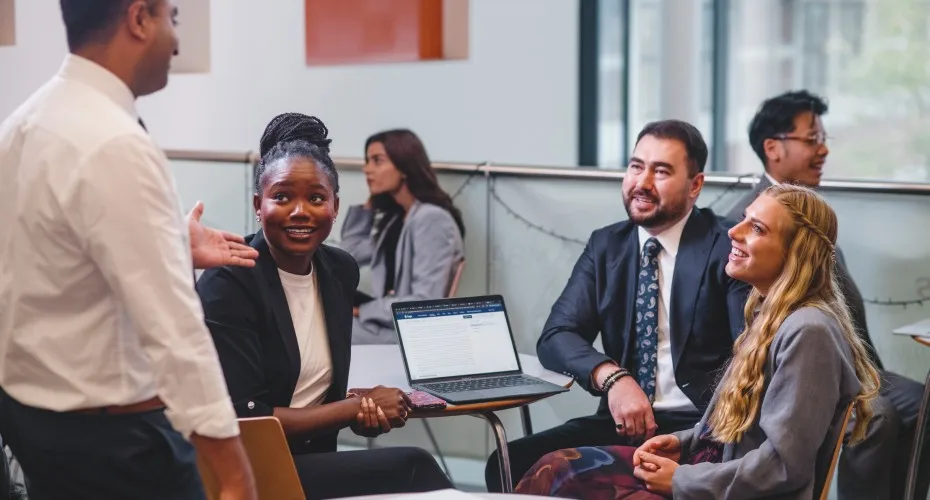 A group of mba students collaborating around a table with laptops during a cohort exercise.