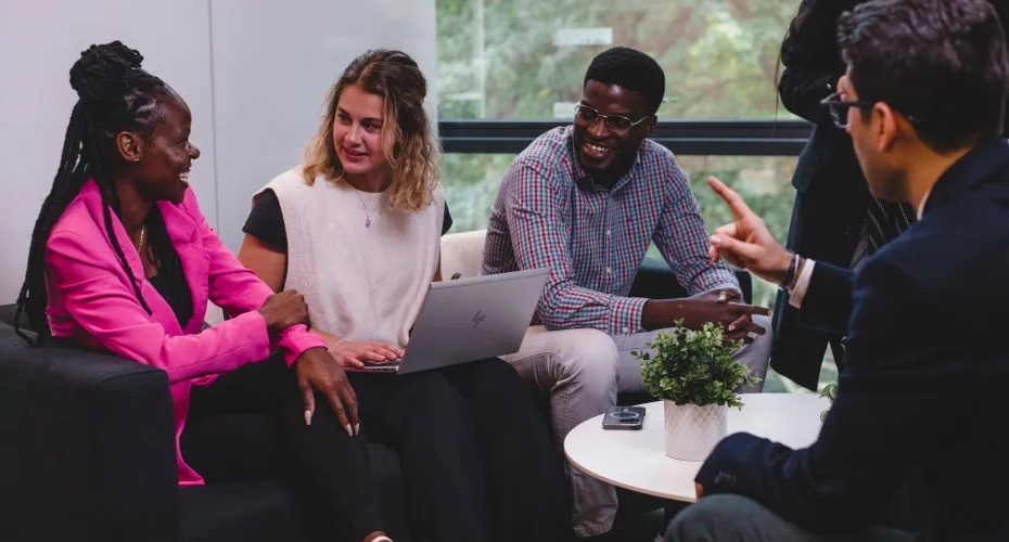 Mba cohort members engaged in group work on laptops, sitting together on a couch in a collaborative setting.