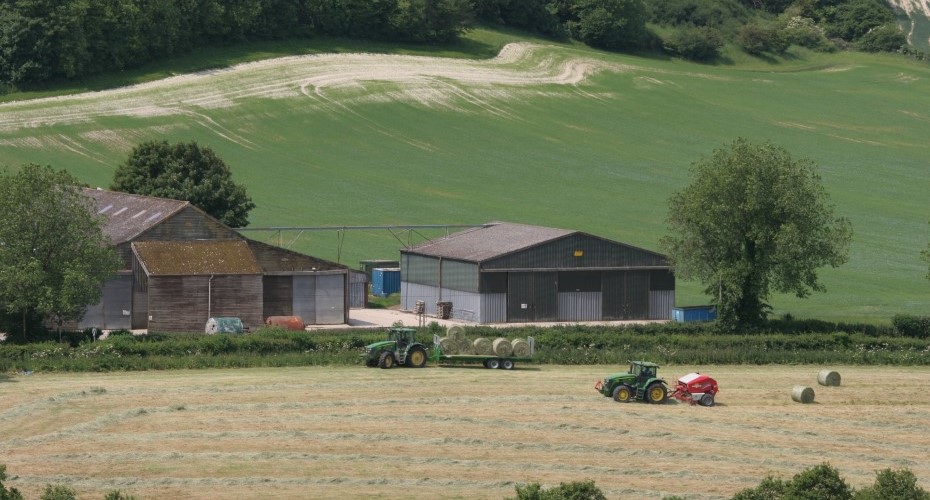 A farm with a tractor and hay bales in the field, showcasing the beauty of rural agriculture.