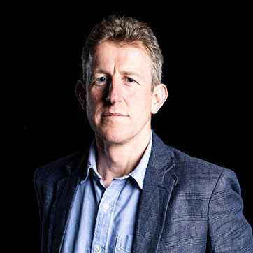 A portrait of Professor Tim Lenton in stark studio lighting, against a dark background.