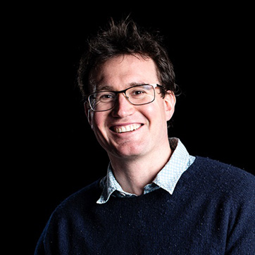 Dr Powell is photographed under studio lighting against the dark background, he's wearing a big smile and looks very approachable