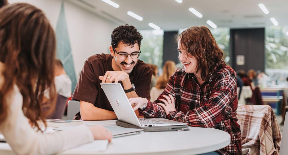 Two students looking at a laptop and smiling in a study space