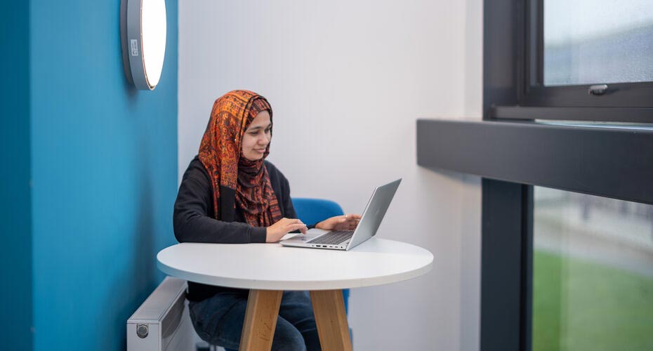 A PhD student sat at a table on campus and working on her laptop
