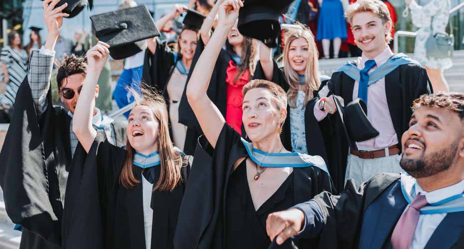 A group of graduates throw their mortarboard hats in the air