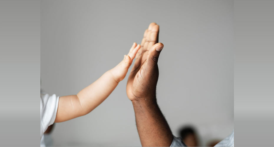 An adult hand high-fiving a baby's hand